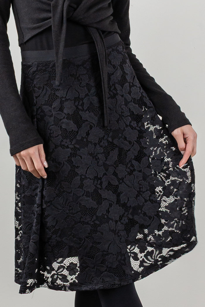 A black lace midi skirt with a matching black waist tie, worn by a model in a studio setting.