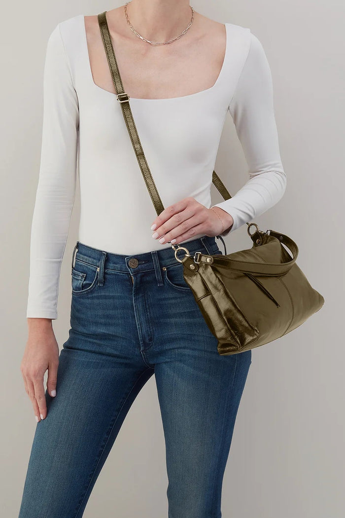 Person wearing a white long-sleeve top and blue jeans, holding a green handbag against a plain background