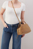 Person wearing a white top and blue jeans holding a brown handbag against a plain background