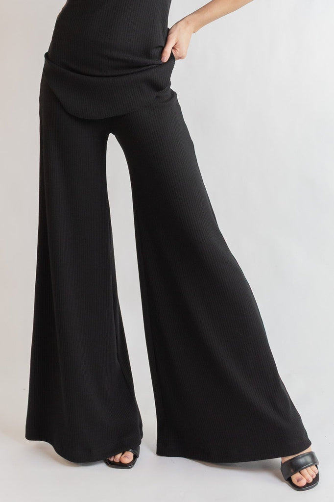 Woman wearing a black sleeveless top and wide-leg pants on a white background