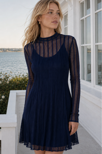 Woman wearing a navy dress with long sleeves by a waterfront.