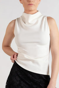 A model wearing a sleeveless white mock-neck top and a black lace A-line skirt, paired with black tights and black boots, against a plain light gray studio background.