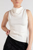 A model wearing a sleeveless white mock-neck top and a black lace A-line skirt, paired with black tights and black boots, against a plain light gray studio background.