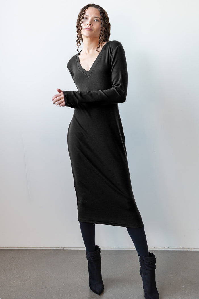 Model is wearing a long sleeve dress in black that is below knee length. 