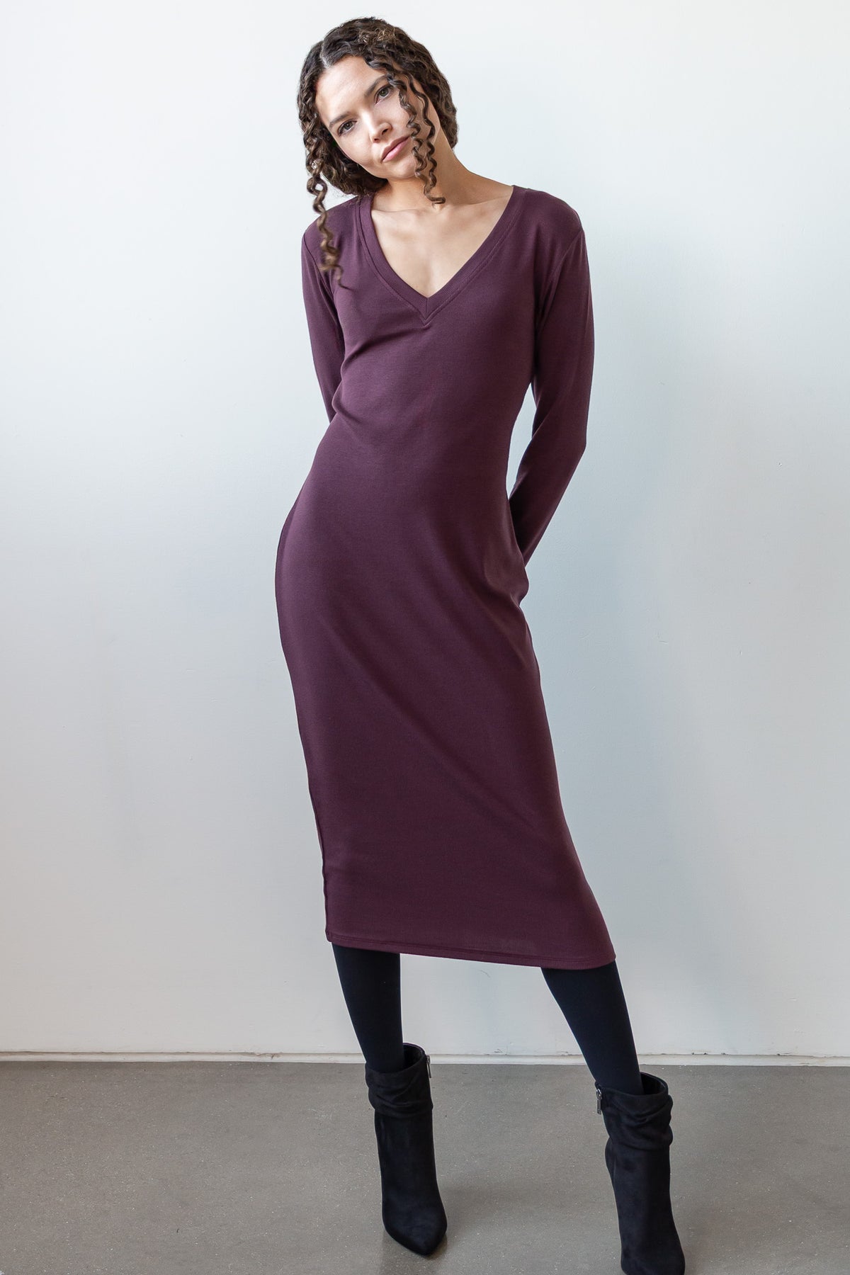 Model is wearing a long sleeve dress in raisin that is below knee length. 