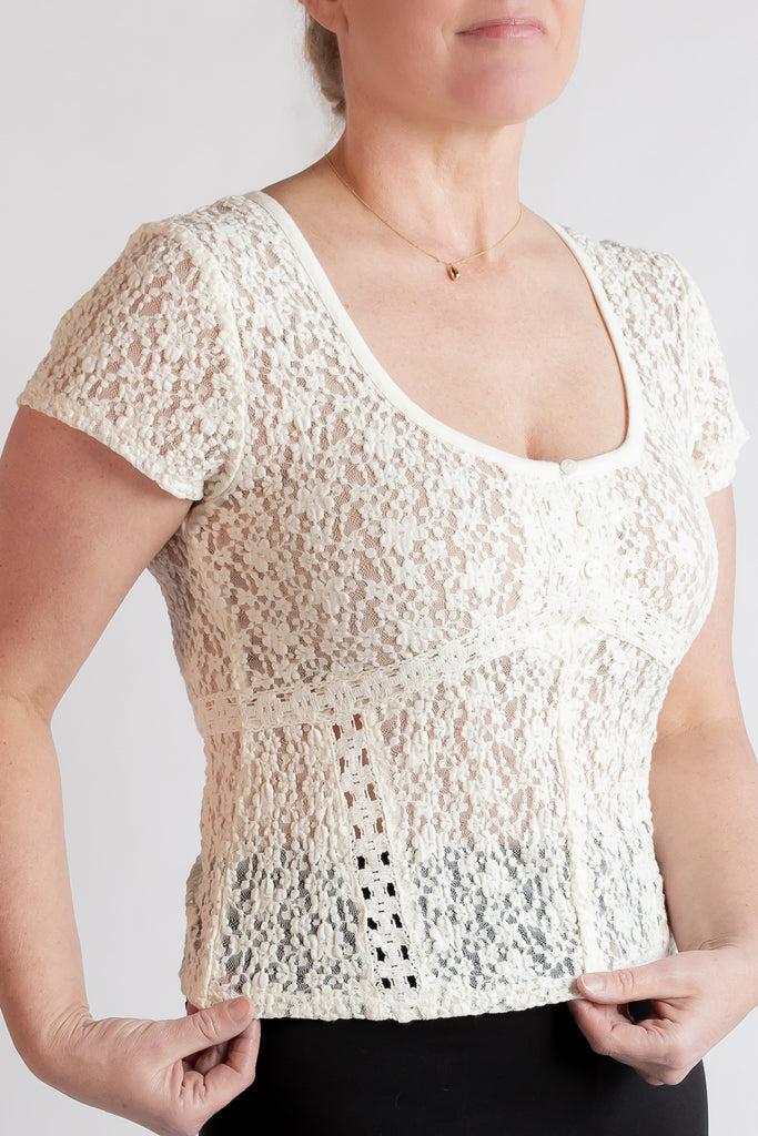 Woman wearing a beige lace top against a plain background