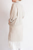 Person wearing a beige and white layered outfit on a plain background