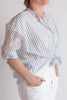 Woman wearing a striped blouse and white pants on a plain background