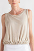 Woman wearing a beige sleeveless top and white shorts on a plain background