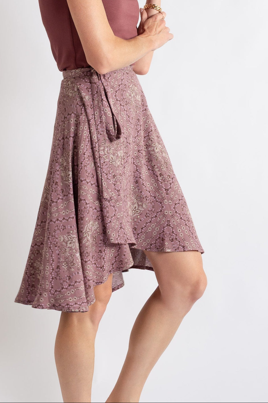 Woman wearing a sleeveless maroon top and floral skirt on a white background