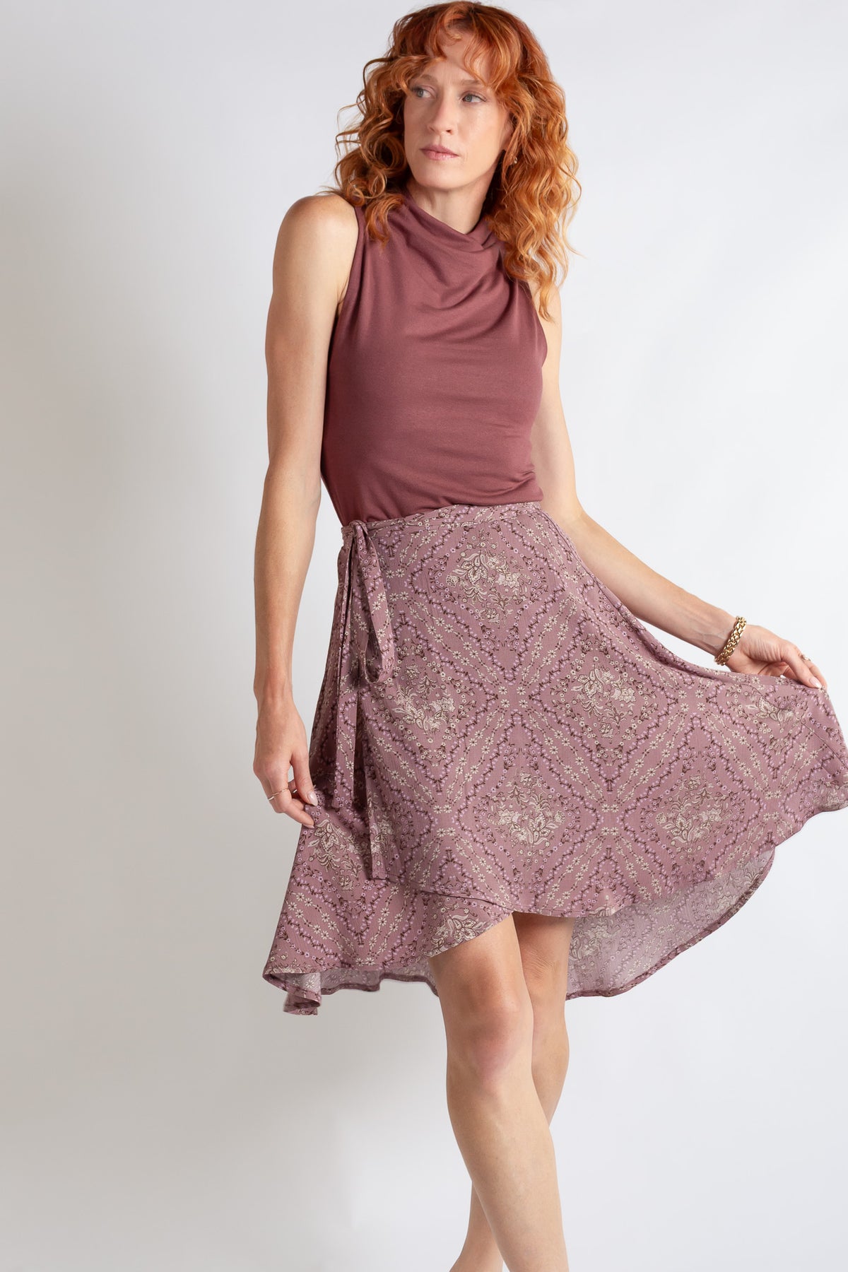 Woman wearing a sleeveless top and floral skirt on a plain background