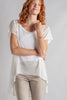 Woman wearing a white top and beige pants against a plain background