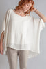 Woman wearing a white poncho and beige pants against a gray background