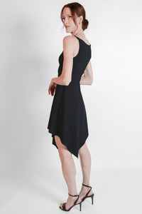 Woman wearing black ribbed fabric dress with an asymmetrical hem. Side view.