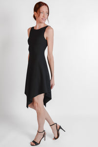 Woman wearing black ribbed fabric dress with an asymmetrical hem. Side view.
