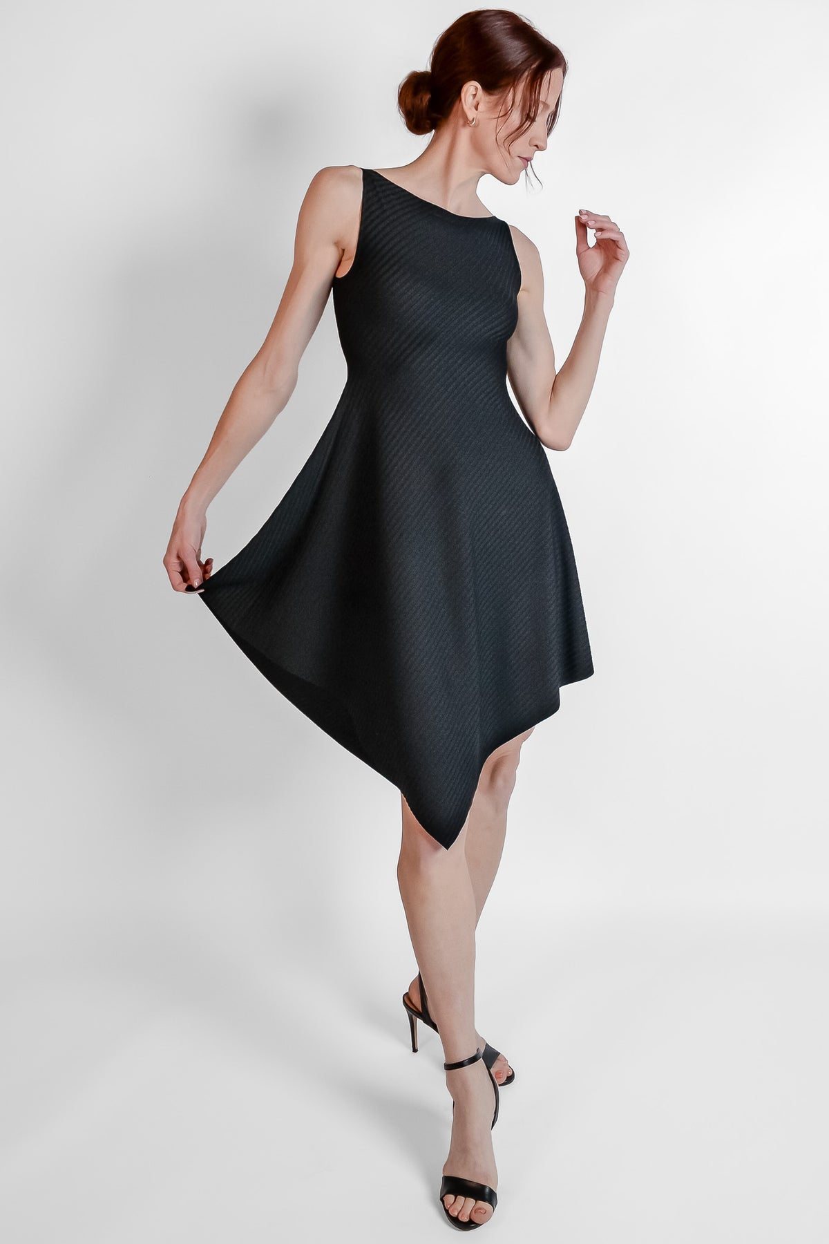 Woman wearing black ribbed fabric dress with an asymmetrical hem. front view.