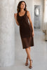 Woman in a brown dress standing against a white wall in a minimalistic room.
