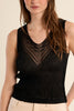 Woman wearing a black sleeveless top with intricate detailing on a beige background