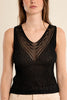 Woman wearing a black sleeveless top with intricate detailing on a beige background