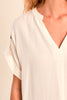 Close-up of a person wearing a light-colored blouse with a V-neckline on a beige background