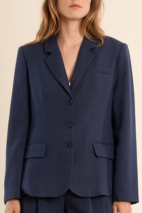 Woman wearing a navy blue suit with a jacket and shorts on a beige background
