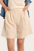 Woman wearing a denim jacket over a cream top and beige shorts on a beige background