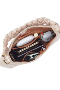 Beige handbag with braided handle and open to reveal beauty products on a white background