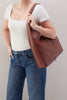 Person holding a brown leather tote bag against a neutral background