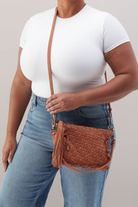 Person wearing a white top and blue jeans holding a brown woven handbag against a neutral background