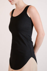 Model wearing the Hedy black Tunic Tank, a ribbed tunic-length tank with curved hem and round neckline, styled for everyday layering